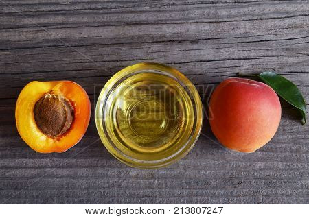 Apricot oil from apricot kernels in a glass bowl and fresh ripe apricots on old wooden background.Essential apricot kernel oil for spa,beauty treatment,aromatherapy and bodycare.Selective focus.