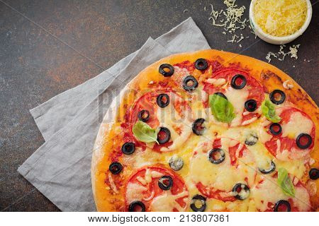 Pizza margarita with tomatoes mazarella and slices of olives on a dark concrete or stone background. Traditional Italian cuisine. Selective focus. Top view.