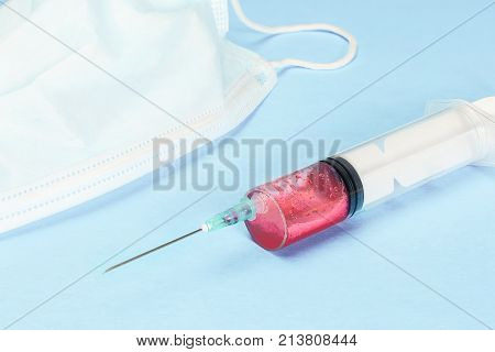 a medical syringe with blood and a medical mask on a blue background