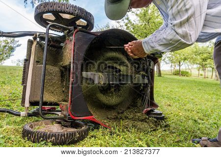 Man cleaning lawn mower blade. Preparing to mow some grass.