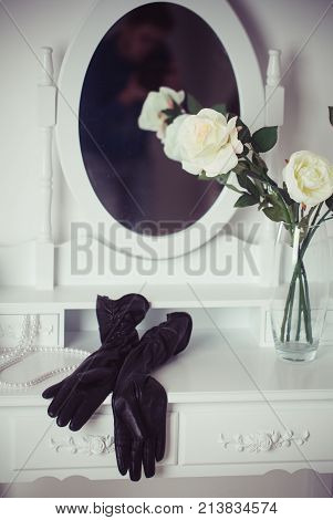 beauty and fashion console mirror with female black leather gloves and white rose flowers in glass vase dresser and boudoir