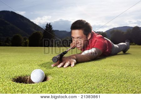 Glada unga manliga golf spelare ligger på green och med golf club som biljard cue (kö) till hål boll