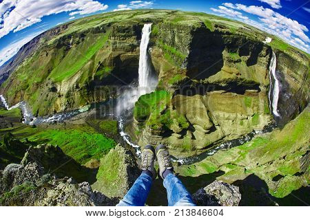 famous Haifoss waterfall in southern Iceland. treking in Iceland. hiker makes selfi by photographing his legs from above. A man is sitting on the edge of a cliff