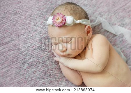 Cute newborn baby girl is sleeping on her side wearing flower headband. Close-up shot.