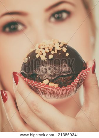 Diet sweets food concept. Woman holding delicious chocolate cupcake with peanut frosting about to take bite