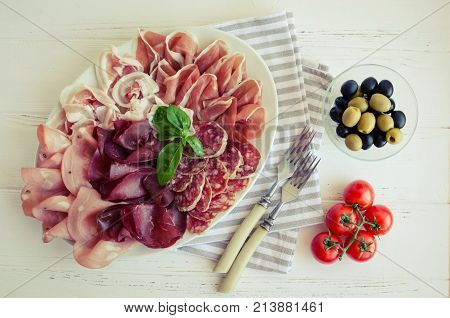 Cold smoked meat plate with pork prosciutto salami bresaola with black and green olives and tomatoes cherry on white wooden background served for two. Wine appetizer set. Italian food. Top view.
