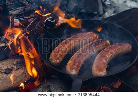 Cooking Sausages In Cast Iron Skillet On Campfire While Camping. Good And Positive Campfire Food.
