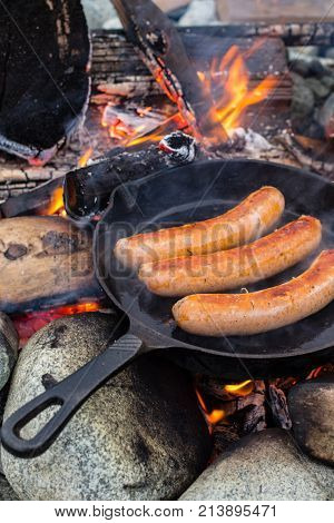 Cooking Sausages In Cast Iron Skillet On Campfire While Camping. Good And Positive Campfire Food.