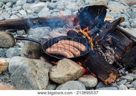 Cooking Sausages In Cast Iron Skillet On Campfire While Camping. Good And Positive Campfire Food.