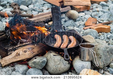 Cooking Sausages In Cast Iron Skillet On Campfire While Camping. Good And Positive Campfire Food.