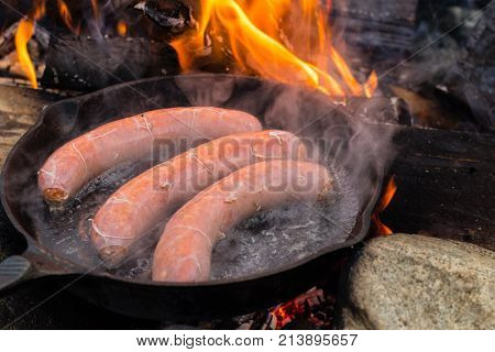 Cooking Sausages In Cast Iron Skillet On Campfire While Camping. Good And Positive Campfire Food.