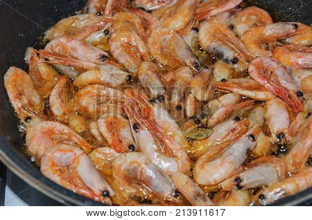 unpeeled shrimp fried in boiling olive oil in a frying pan