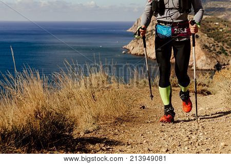 athlete runner with trekking poles running mountain trail along sea