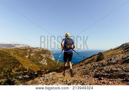 back male athlete runner running mountain trail with hiking sticks