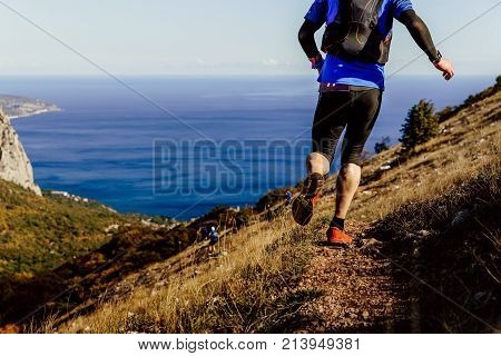 back legs of male athlete running mountain trail in background sea