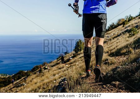male runner running mountain trail with hiking sticks in background sea