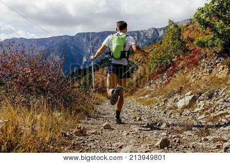 male runner running mountain trail on background autumn forest with trekking poles