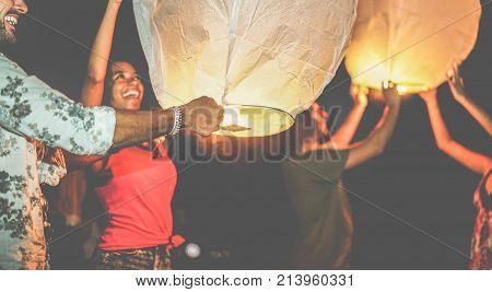 Happy friends lighting sky lantern on the beach in the night - Young people having fun in asian floating lamps festival - Travel vacation and fest concept - Focus on man hand - Contrast filter