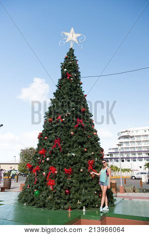 Cozumel Mexico - January 13 2016: girl at christmas tree with star red bow decorations ornaments outdoor on blue sky. New year xmas holiday celebration vacation concept