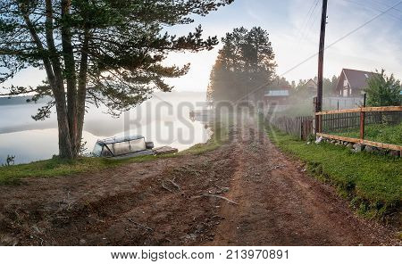 summer early morning on the lake in the fog. against the background of the mountains and the village on the shore. one fishing boat lie on the beach in the background of a pink dawn