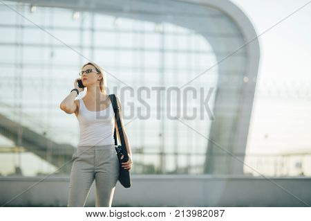 Attractive business woman using a phone and clock while standing in front of windows in an office building overlooking the city