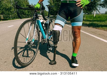 Athlete With Disabilities Or Amputee Training In Cycling In Sunny Summers Day. Professional Male Spo