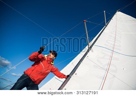Low Angle View Of Sailor Operating Windlass On Yacht. Working With Ropes And Sail