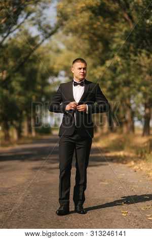 Young Man Walking In The Park. Handsome Groom In Black Suit