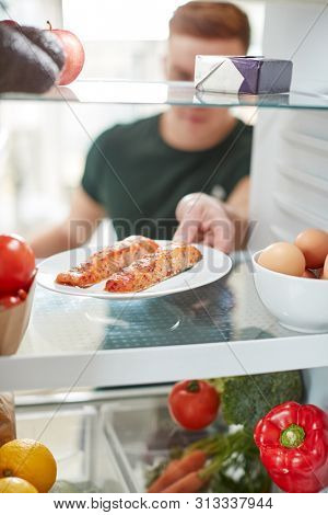 Young Man Reaching Inside Refrigerator Of Healthy Food For Fresh Salmon On Plate