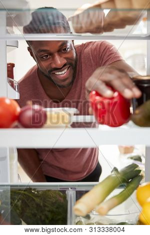 View Looking Out From Inside Of Refrigerator As Man Opens Door And Unpacks Shopping Bag Of Food