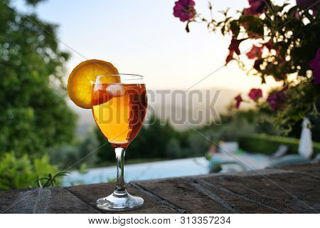 Spritz Veneziano Cocktail Drink On A Garden Wall In Front Of An Idyllic Landscape, Sunset Sky With C