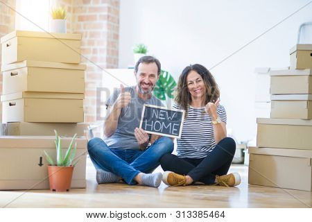 Middle age senior couple sitting on the floor holding blackboard moving to a new home happy with big smile doing ok sign, thumb up with fingers, excellent sign
