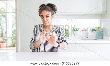 Beautiful african american woman with afro hair wearing casual striped sweater disgusted expression, displeased and fearful doing disgust face because aversion reaction. With hands raised. 