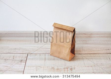 Paper Bag On Light Wooden Floor. Simple Brown Paper Bag For Lunch Or Meal. The Layout For The Design