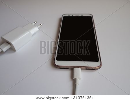 A Smartphone With A White Usb Cable For Charging