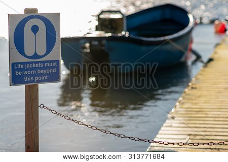 Warning Sign That Says Life Jackets Must Be Worn Beyond This Point With A Boat In The Background On 