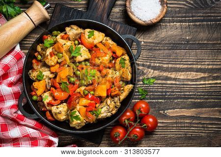 Chicken Stir Fry With Vegetables In The Black Iron Plate. Top View On Dark Wooden Background.