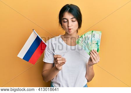 Young caucasian woman holding pills making fish face with mouth and squinting eyes, crazy and comical. 