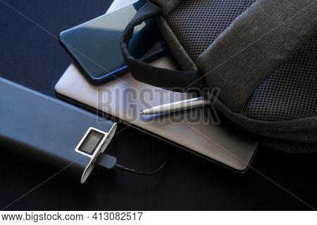 A Large External Battery - Power Bank With Display Lies On The Table Next To A Gray Textile Backpack