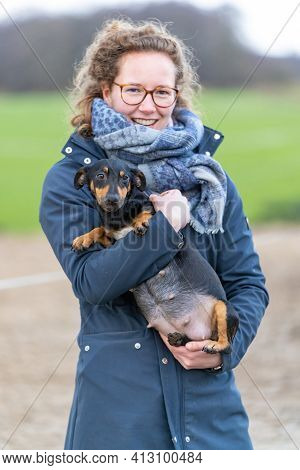 A Smiling Woman Holds A Pregnant Jack Russel Terier In Her Arms. The Dogs Big Belly Can Be Seen Clea