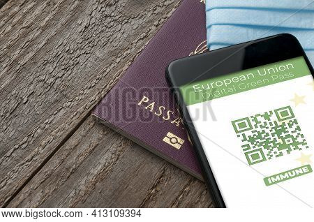Digital Green Pass Concept: Smartphone Over A Passport And A Surgical Mask On A Wooden Table Show An