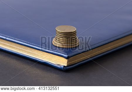 Blue Diary And Stack Of Coins On A Black Background. Planning. Business Concept
