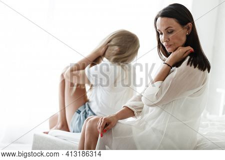 Family conflict and relations concept. Mother and daughter having quarrel and aguring at home. Sad woman and teenage girl sitting on bed. Not looking at each other.
