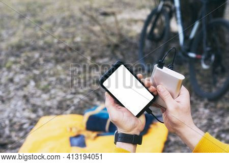 The Cyclist Holds A Mock-up Of A Smartphone With A White Screen In His Hand And Charges It With A Ba