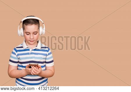 Cheerful Young Boy Listening To The Music In Headphones And Mobile Phone. Smiling Boy Using Smartpho