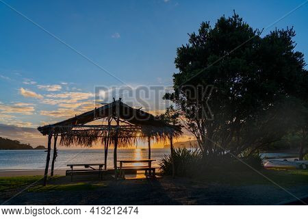 Thatch Roof Shelter On Mulberry Grove Beach Silhouetted Against Golden Sunset On Great Barrier,