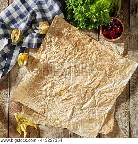 Baking paper with food ingredients. Wooden table at kitchen with baking utensil and fresh vegetables. Crumpled parchment or baking paper as a creative copy space. Top view