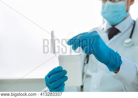 Doctor In Protective Gloves Takes Out A Wet Wipe From The Container .