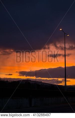 Spectacular Red Sunset With Dark Rainy Clouds Over The Bridge With Silhouettes Of People And Vehicle