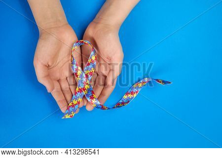 World Autism Awareness Day. Autistic Boy Hands Holding Puzzle Pattern Ribbon On Blue Background